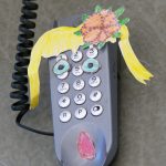 EIn altes Telefon wurde mit Zeichnungen beklebt. Es scheint nun ein Kopf mit Haaren und Augen zu sein.