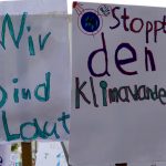 Man erkennt zwei Plakate. Auf dem linken steht "Wir sind laut!", auf dem rechten "Stoppt den Klimawandel!".